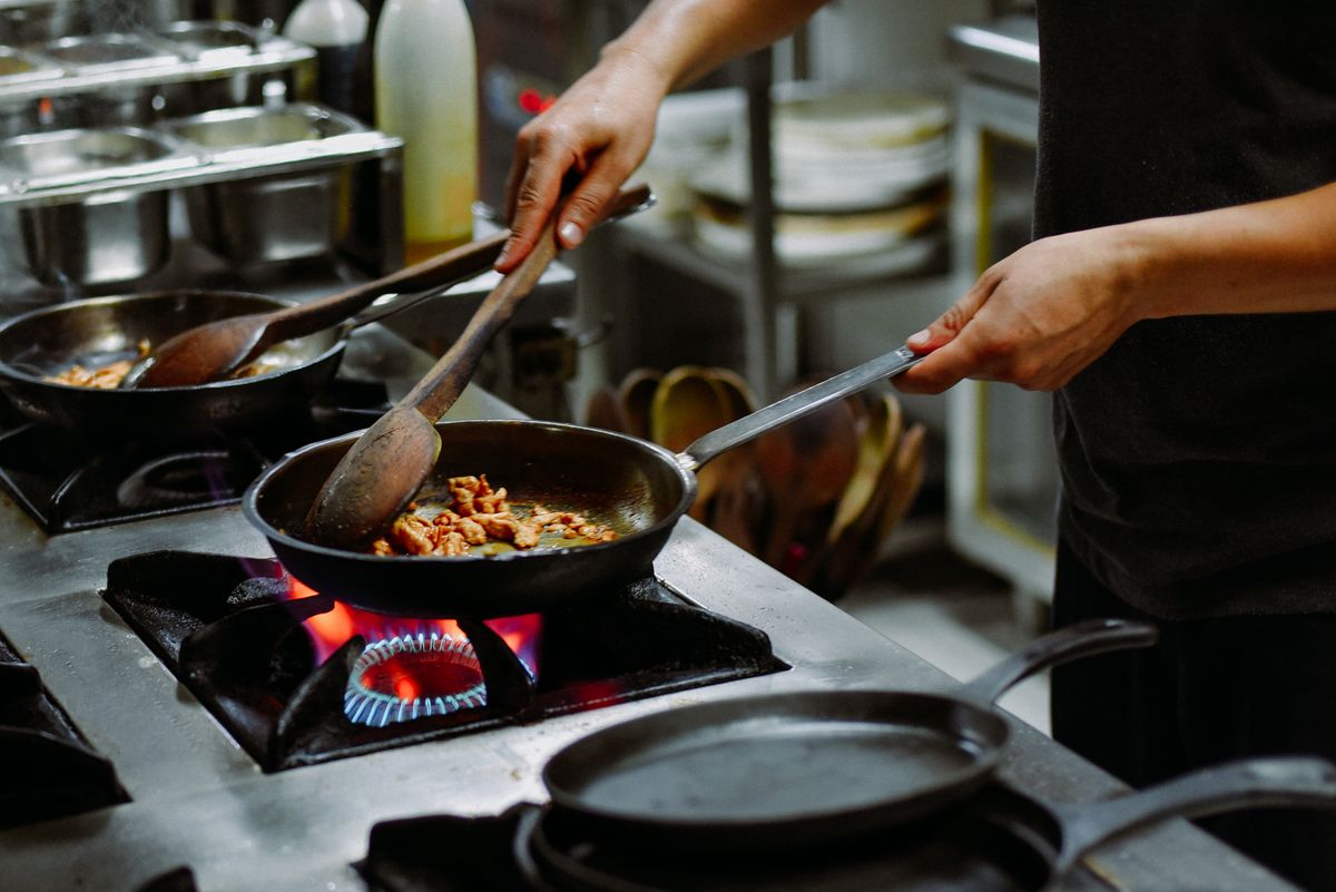 Chef preparing a dish with sautéed ingredients in a restaurant kitchen.