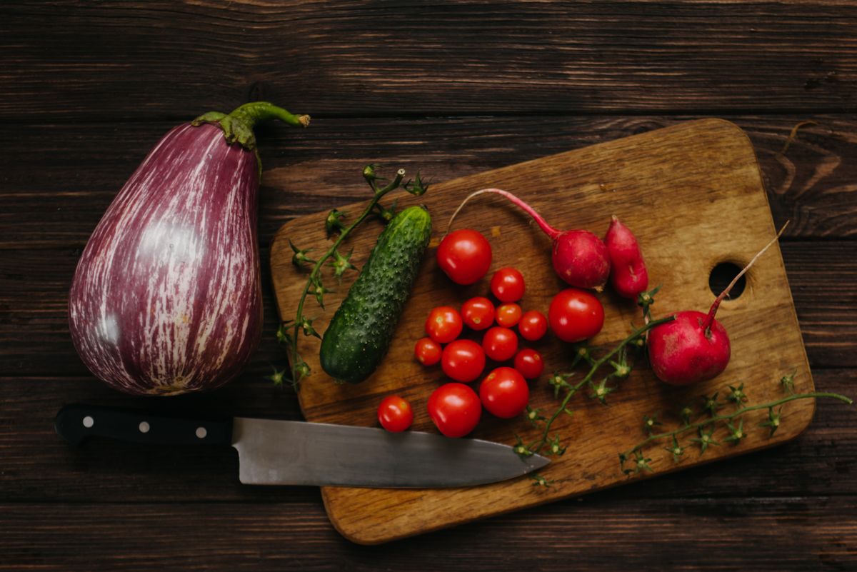 A variety of fresh vegetables with a knife on a rustic wooden cutting board.
