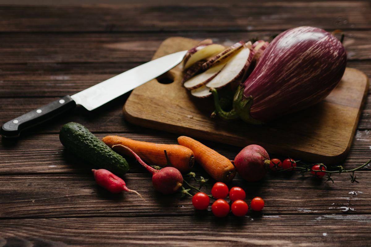 Colorful assortment of fresh vegetables on a wooden board with a knife, perfect for cooking.