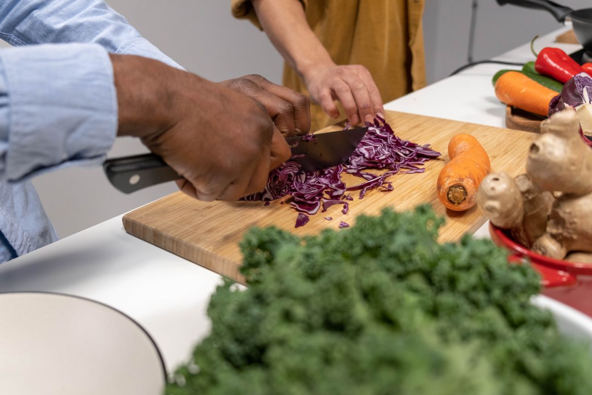 Hands chopping red cabbage on a wooden board with fresh vegetables, emphasizing healthy cooking.