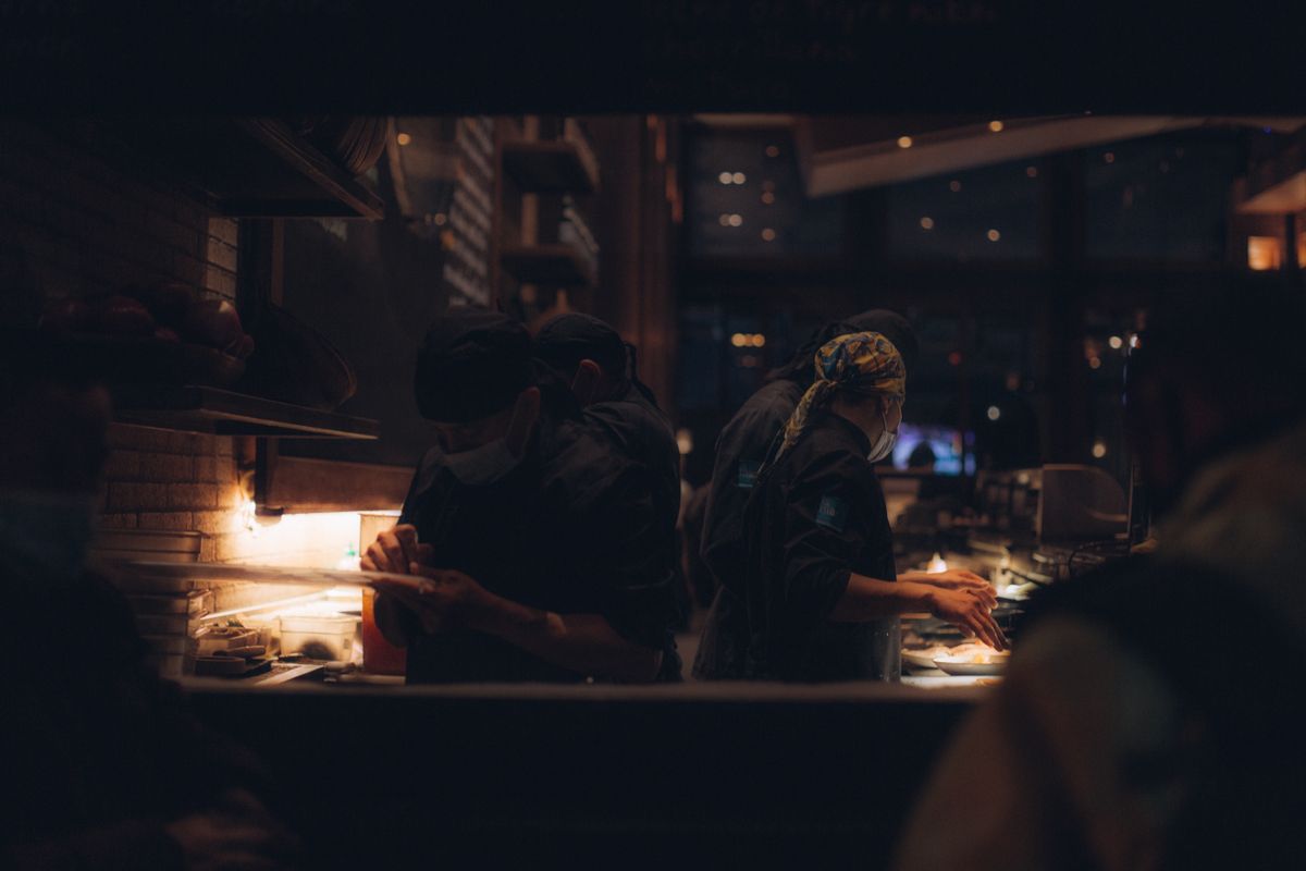 Chefs wearing face masks focused on food preparation in a cozy restaurant kitchen.