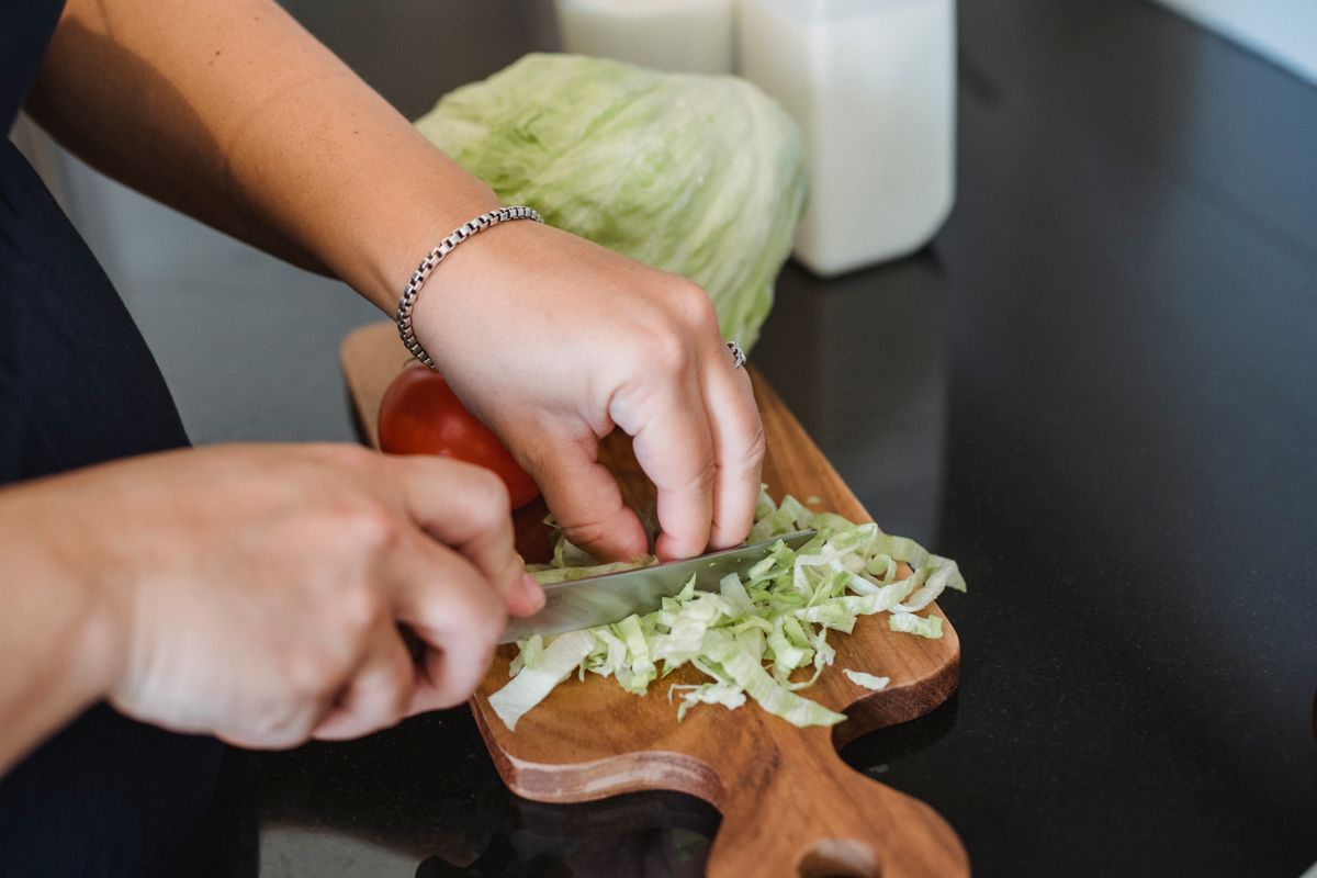 Crop unrecognizable woman cutting fresh green lettuce leaves while preparing healthy salad in kitchen at home
