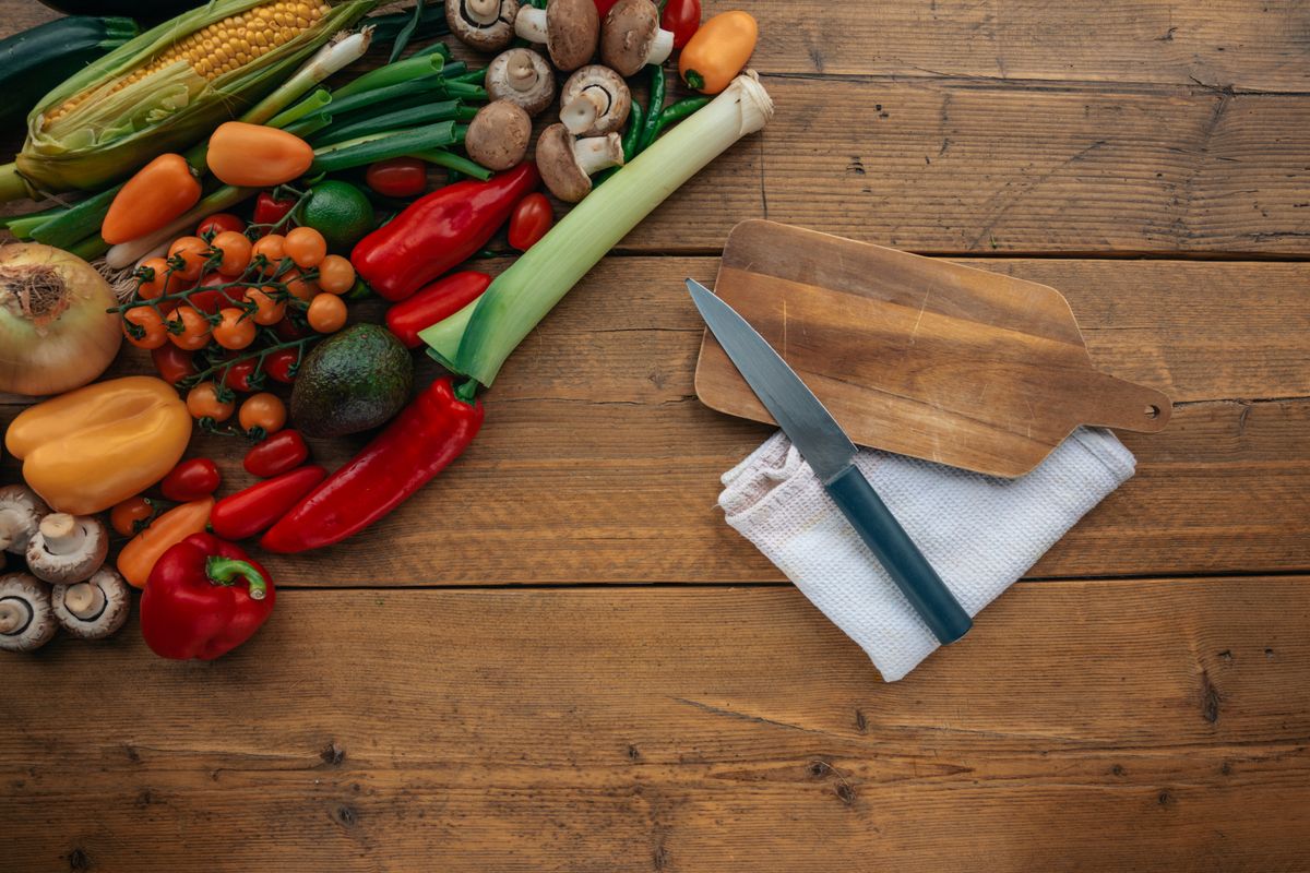 A vibrant assortment of fresh vegetables on a rustic wooden table with a chopping board and knife.