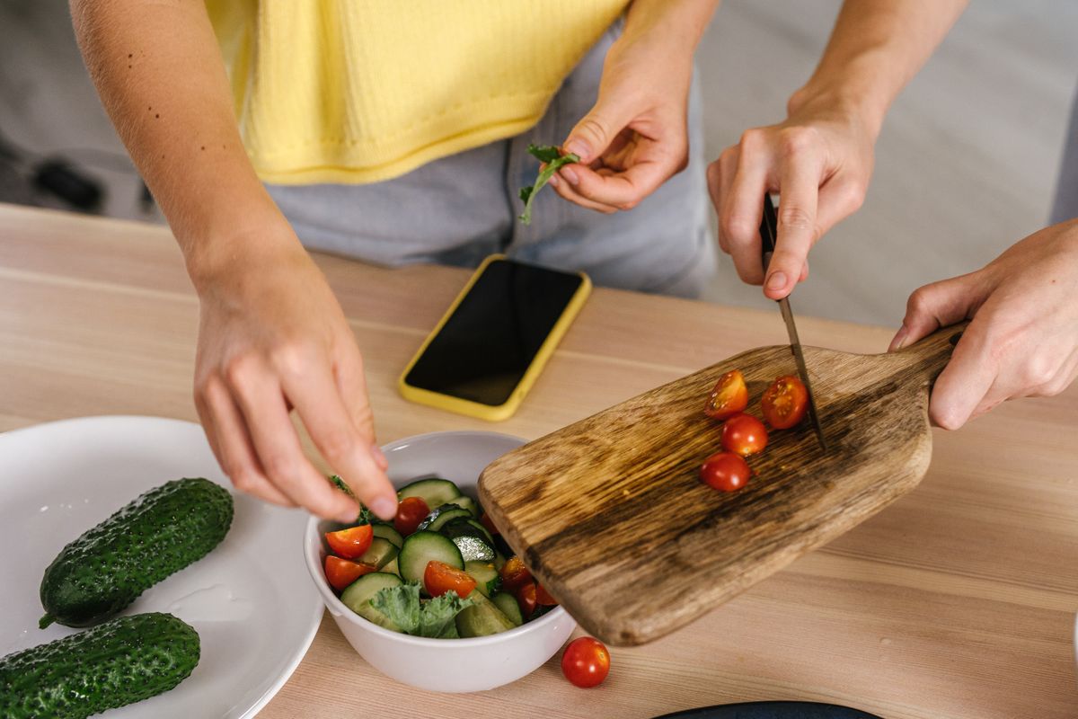 A close-up shot of hands cutting fresh vegetables for a salad on a wooden chopping board indoors.