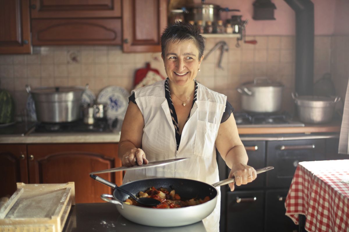 A cheerful woman cooking a meal in a cozy, rustic kitchen setting.