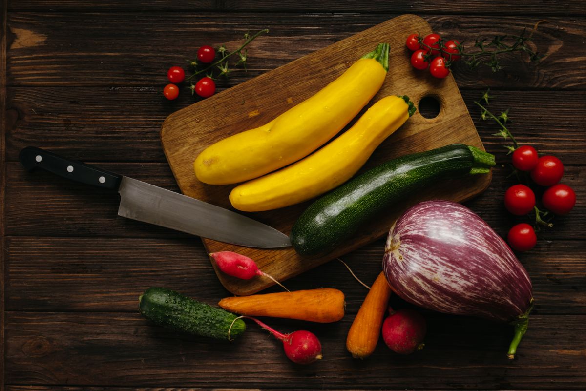 Top view of assorted fresh vegetables on a wooden cutting board with a kitchen knife.