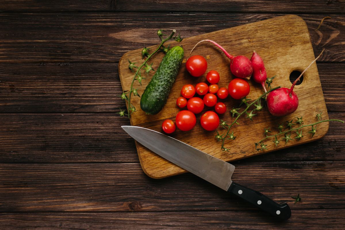 Assorted fresh vegetables including cherry tomatoes, cucumbers, and radishes on a wooden board with a kitchen knife.