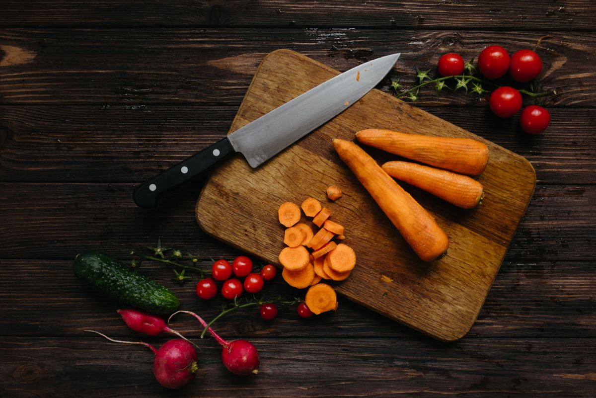 High-angle shot of fresh vegetables and kitchen knife on wooden board.