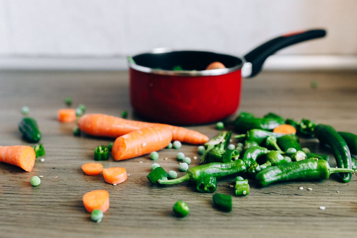 Assorted fresh vegetables including carrots and peppers on a kitchen counter with a cooking pot.