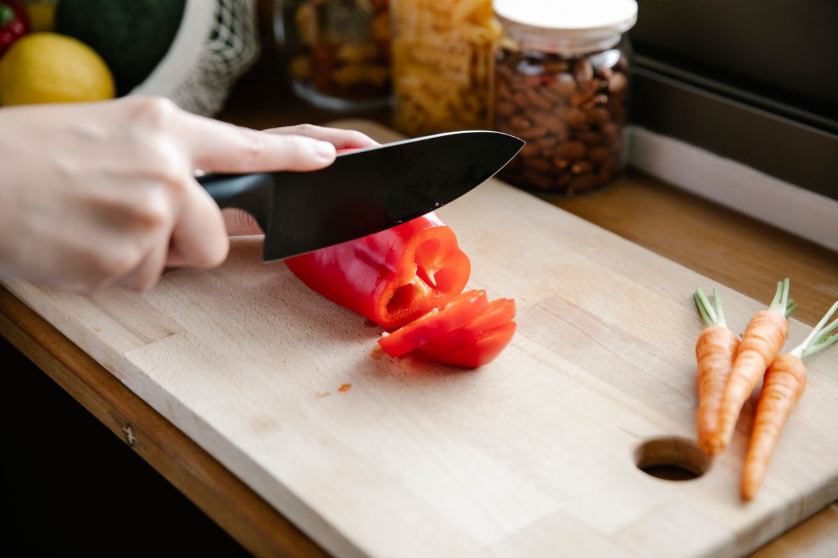 Crop anonymous person slicing ripe fresh red capsicum on chopping board on kitchen counter