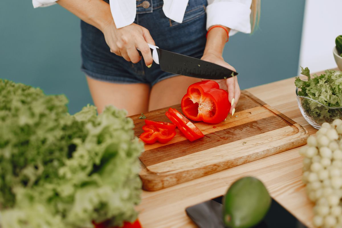 Healthy cooking with fresh red pepper, lettuce, and avocado in a kitchen setting.