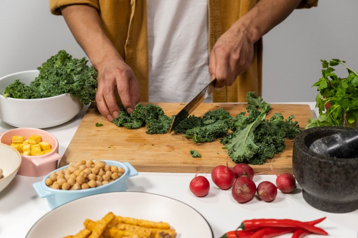 A person chops fresh kale surrounded by vibrant vegetables for a healthy meal preparation in a kitchen.
