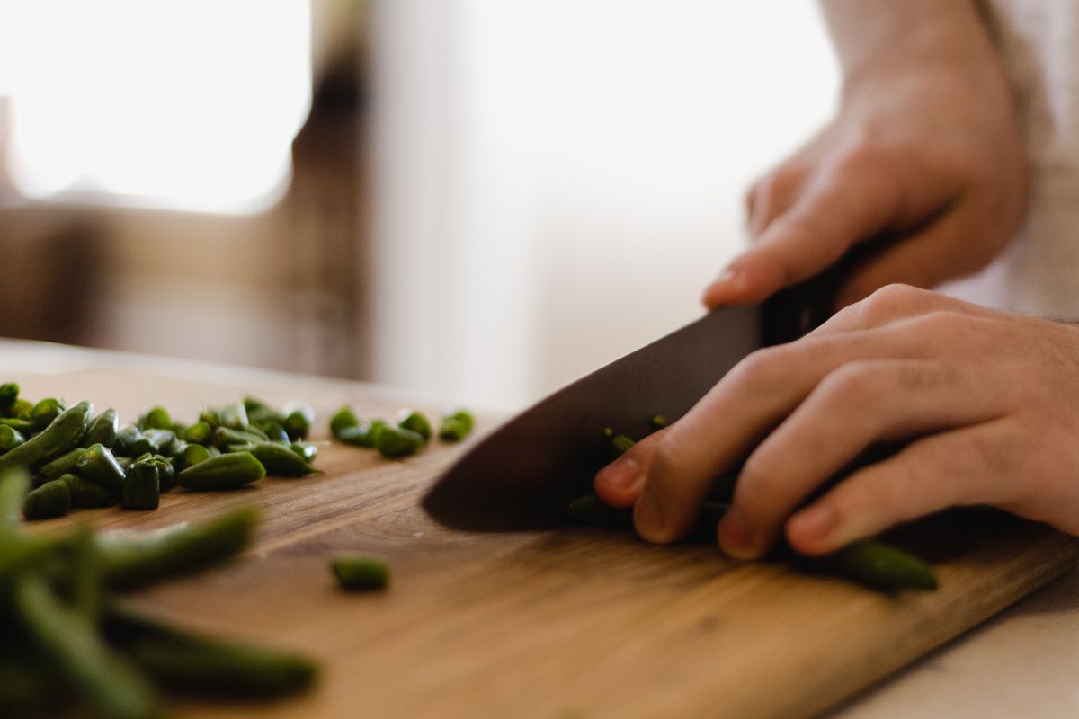 A person slicing fresh green beans with a knife on a cutting board, showcasing food preparation.