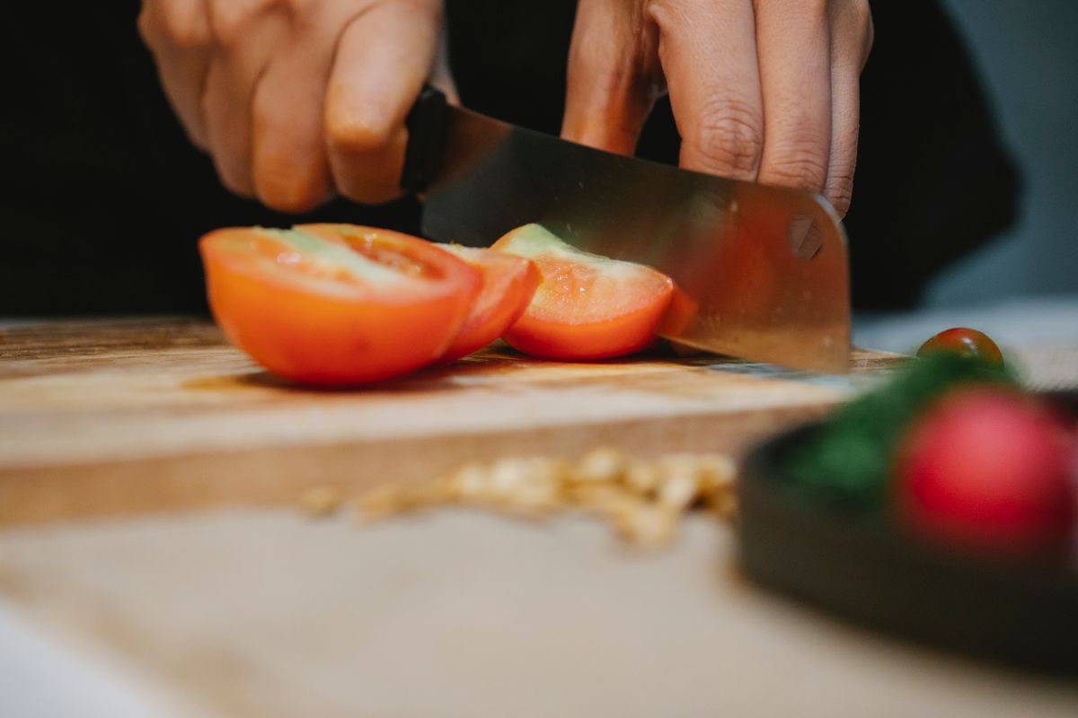 Crop unrecognizable person cooking dish and cutting fresh tomatoes on chopping board in kitchen