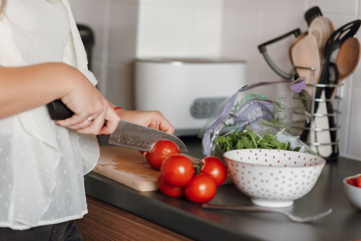 Crop anonymous housewife in casual clothes cutting fresh ripe tomatoes with sharp knife on wooden cutting board while cooking in kitchen