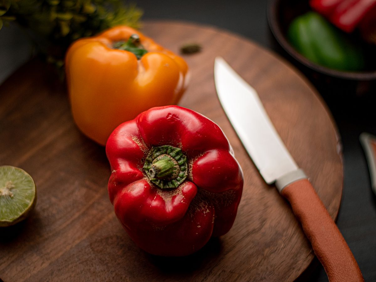 Fresh red and yellow bell peppers on a wooden cutting board with a kitchen knife.