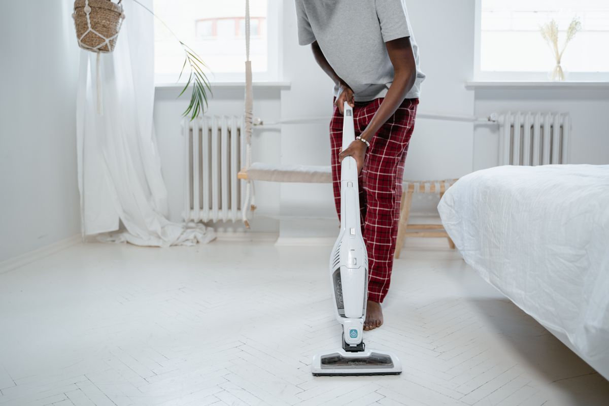 Man cleaning a room with a vacuum cleaner, barefoot in pajamas, ensures tidiness.