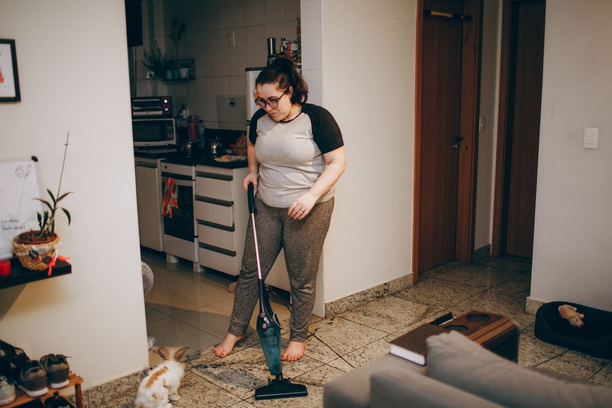 A woman cleaning her living room with a vacuum cleaner while her pet rabbit watches.