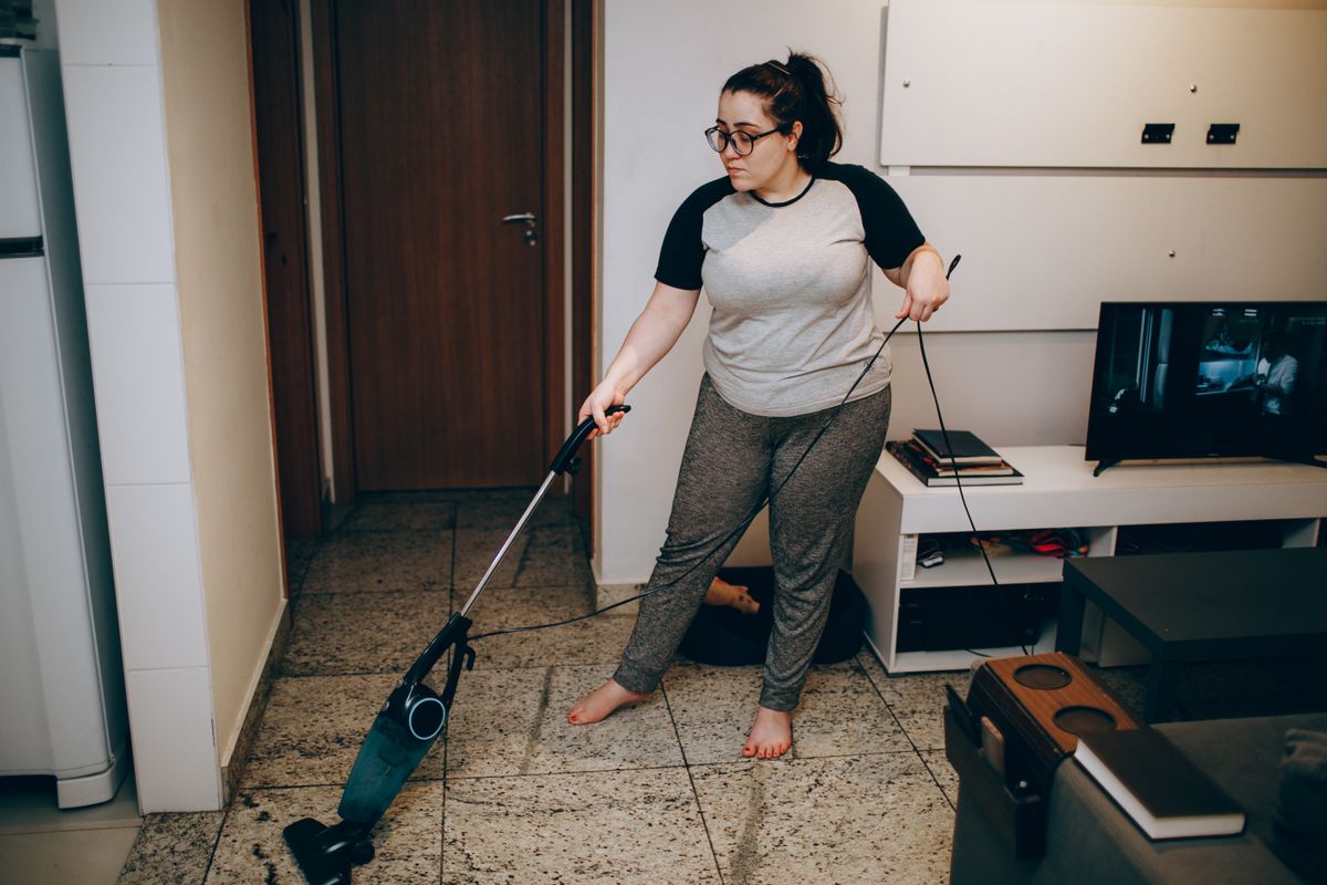 An adult woman cleaning her living room with a vacuum cleaner indoors.