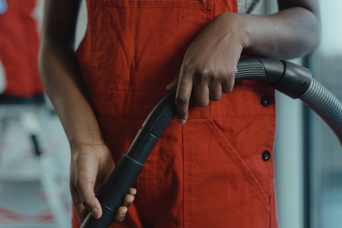 A person in a red apron holding a vacuum cleaner hose during indoor cleaning.
