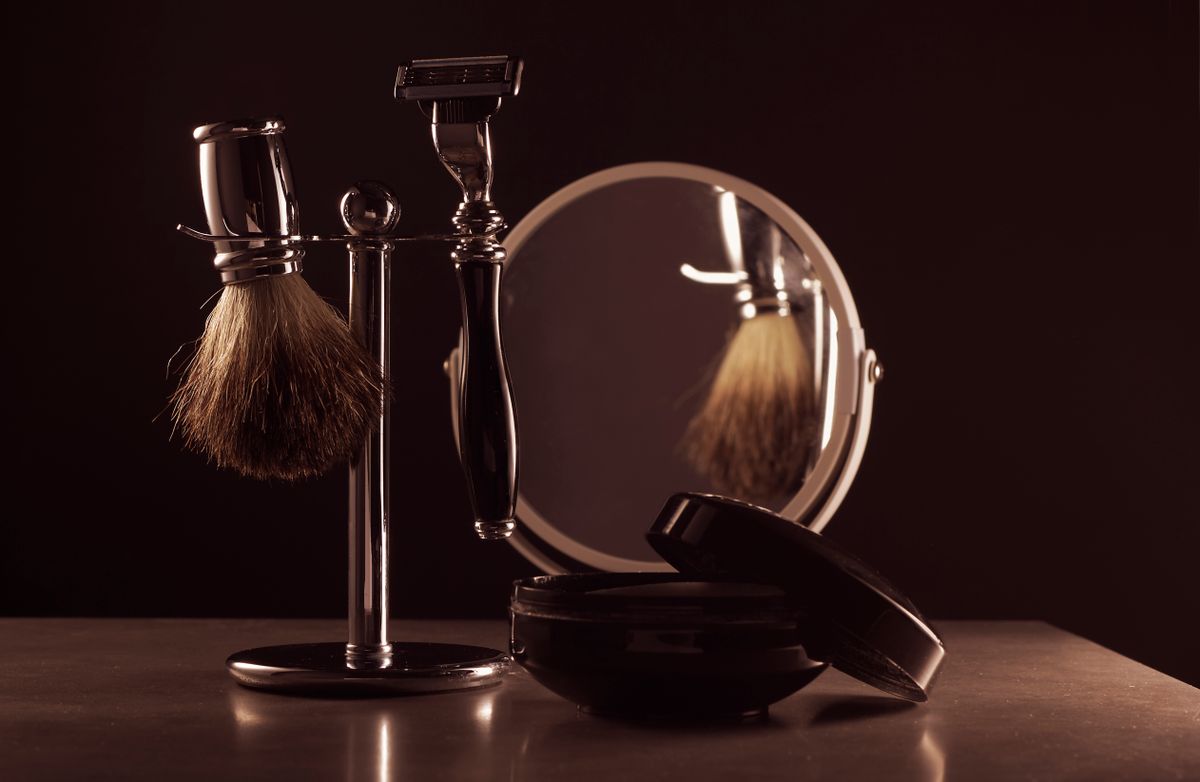 Stylish shaving set featuring a brush, razor, and mirror on a table, ideal for men's grooming.