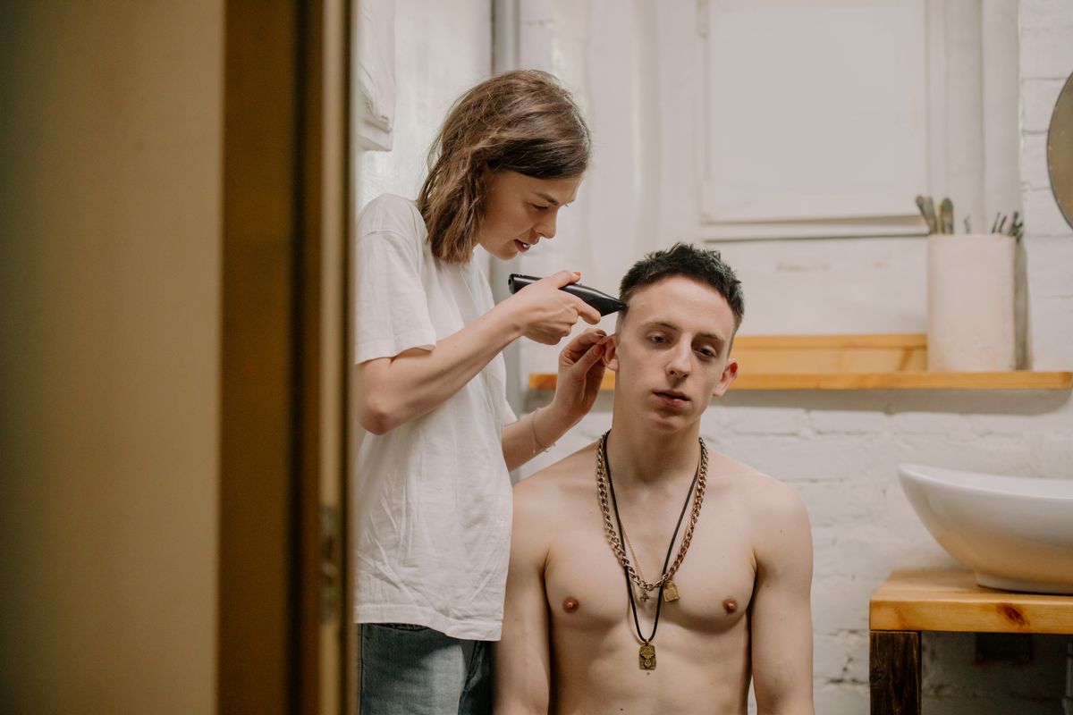 Woman giving a young man a haircut at home, highlighting DIY haircare and grooming.