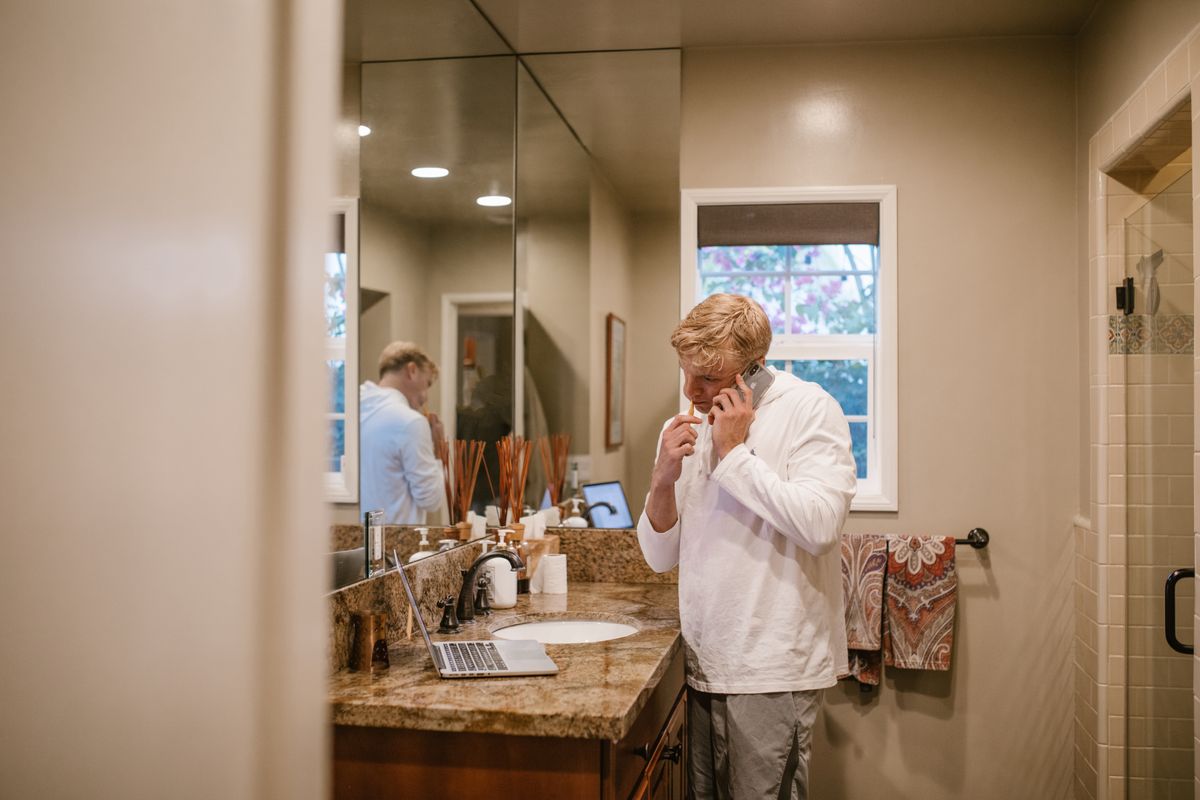 Man multitasking in bathroom, brushing teeth while on phone, reflecting daily routine.