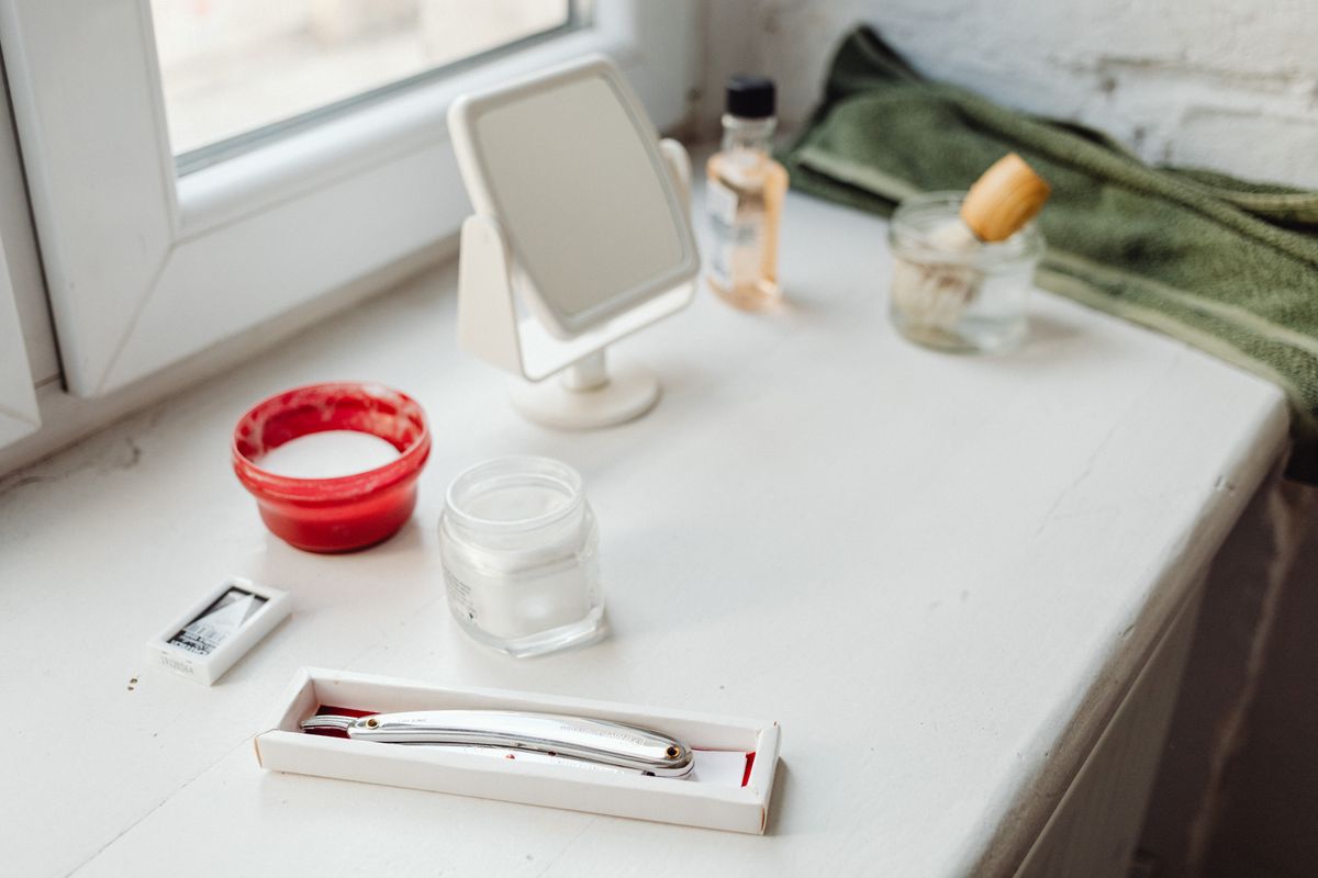 A traditional shaving kit with a razor, brush, and mirror on a bathroom counter.