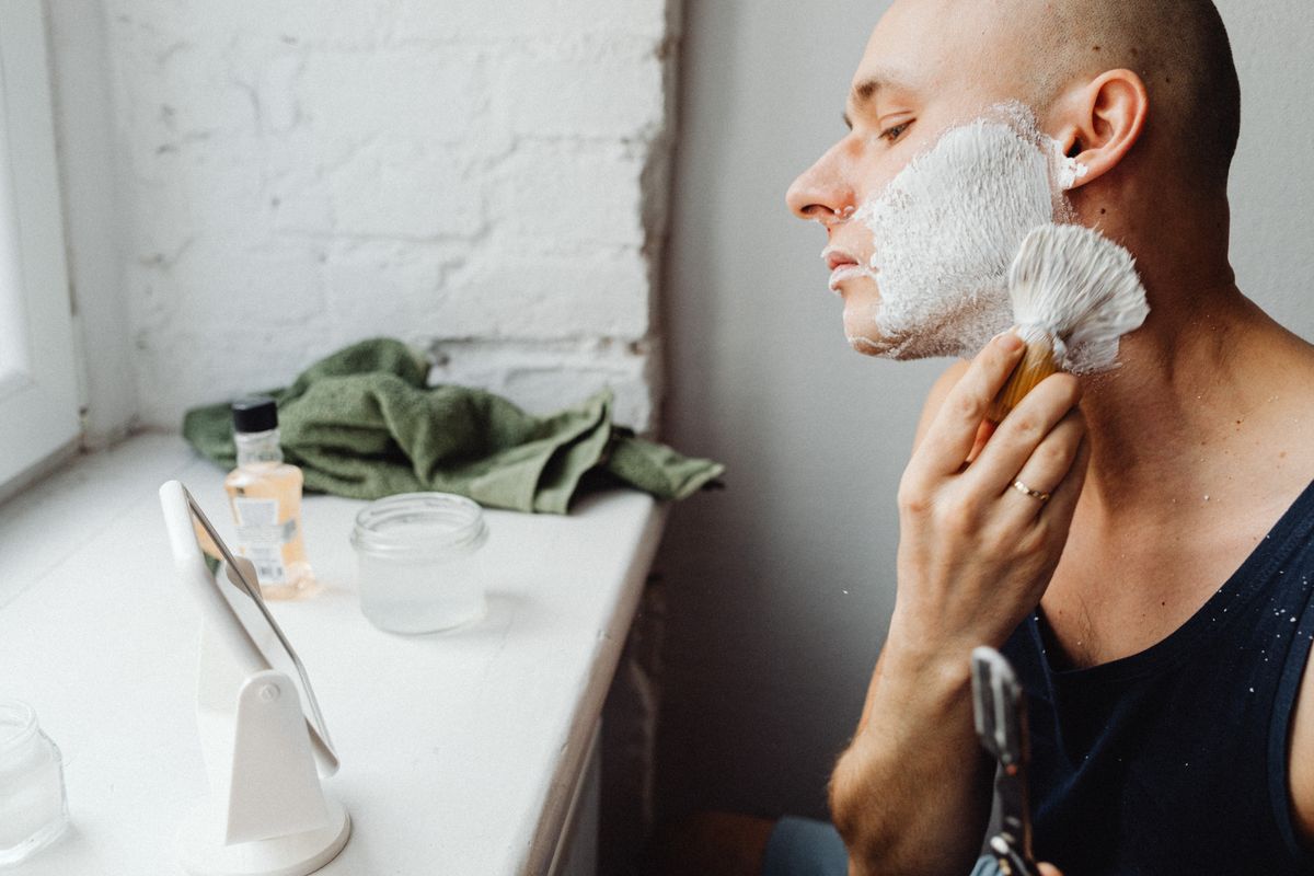 Young man shaving with a brush in front of a mirror. Personal grooming and skincare.