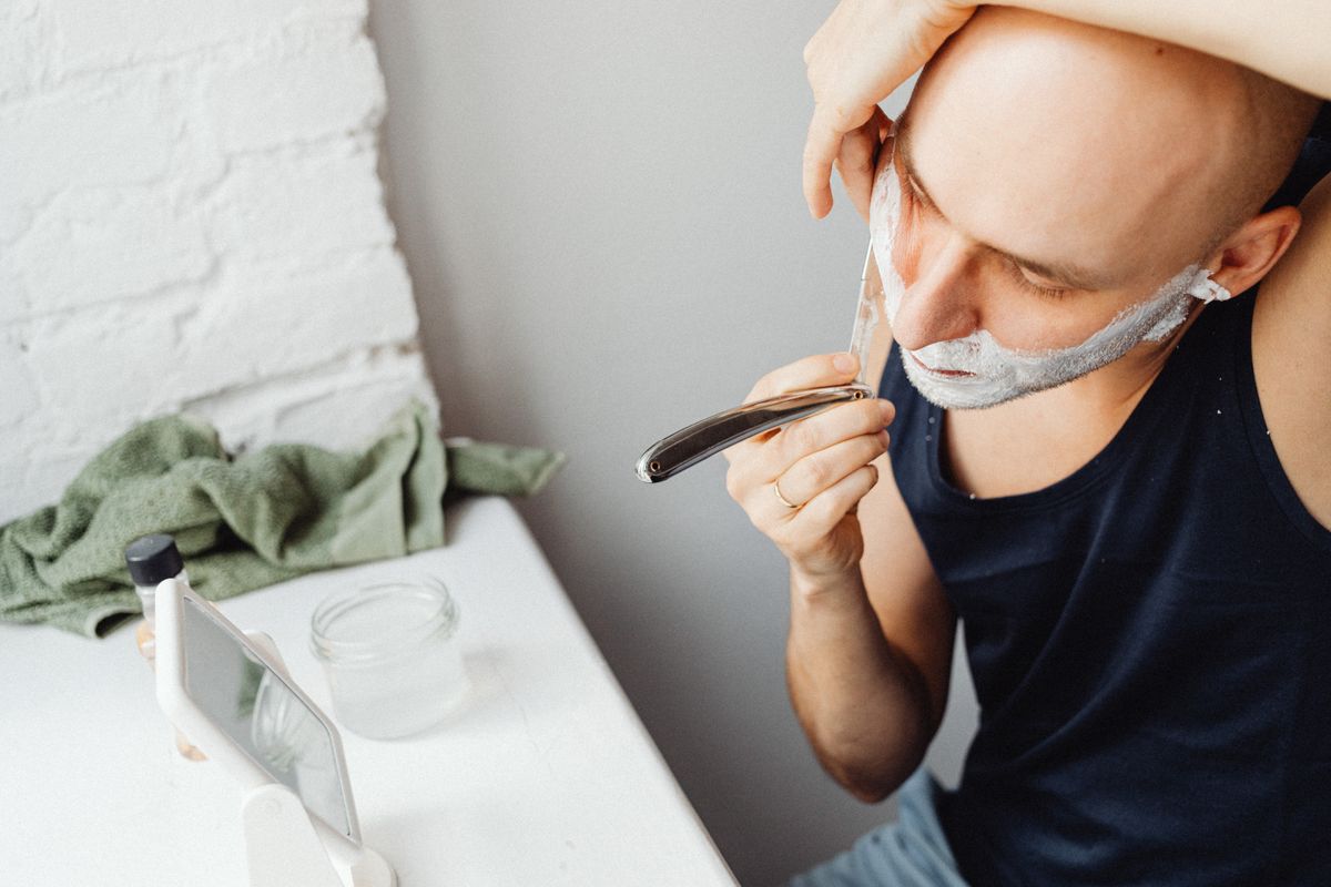 Bald man using straight razor and shaving cream in an indoor setting.