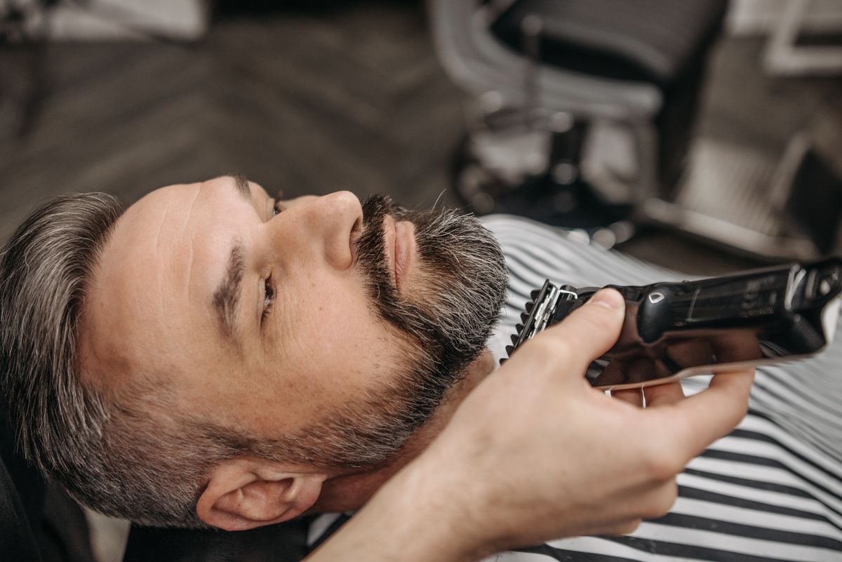 Close-up of a man getting a beard trim at a barbershop with a hair clipper.