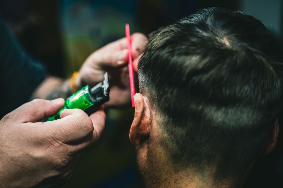 A barber precisely cuts hair with a trimmer and comb, capturing a detailed grooming scene.