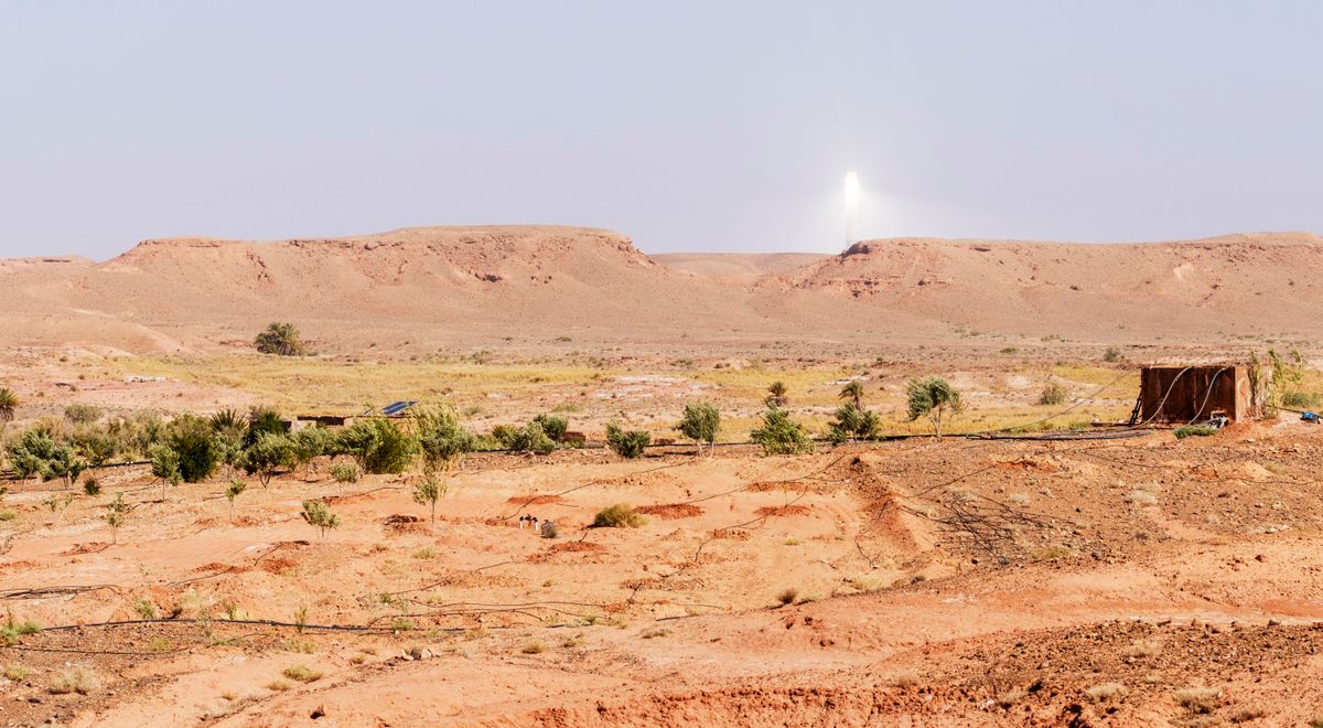 A scenic view of a solar power tower amidst the arid landscape of Morocco's desert with clear skies.