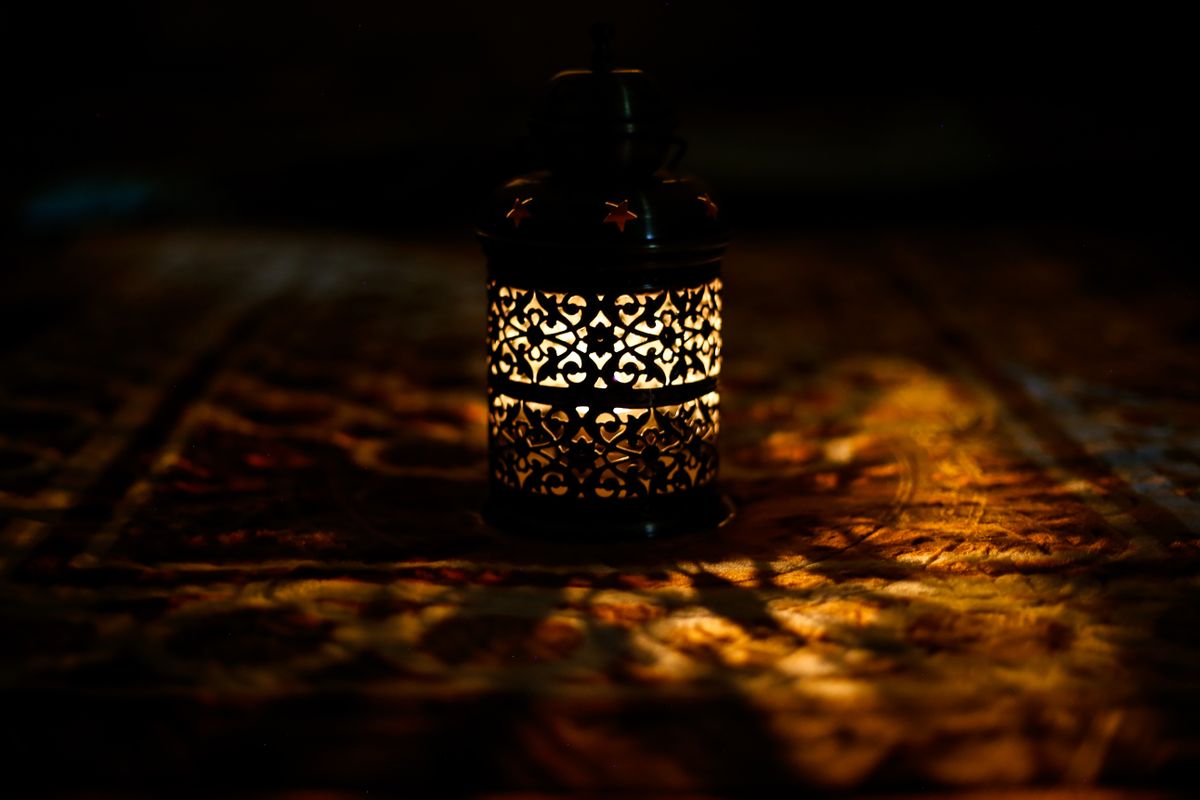 A beautifully intricate lantern casting warm light patterns on a Persian rug in a dark room.