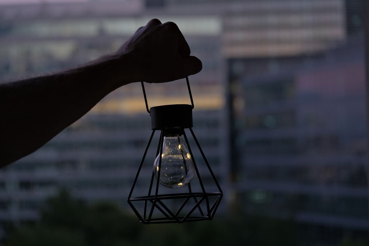 Silhouette of a hand holding a lantern against an urban twilight skyline, representing creativity and light.