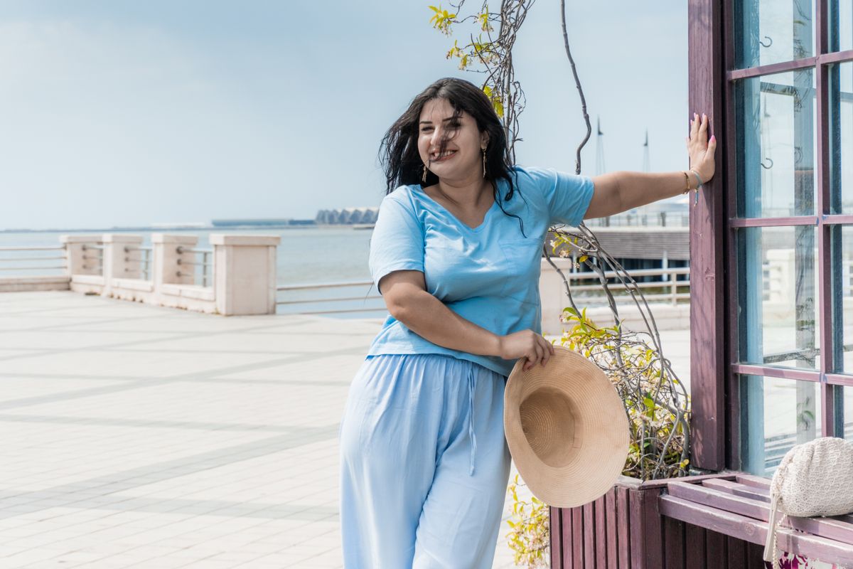 Smiling woman in blue outfit at Baku promenade holding a straw hat.