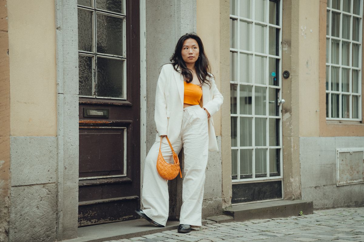 Stylish woman in a white suit and orange crop top posing in an urban setting. Perfect for fashion shoots.