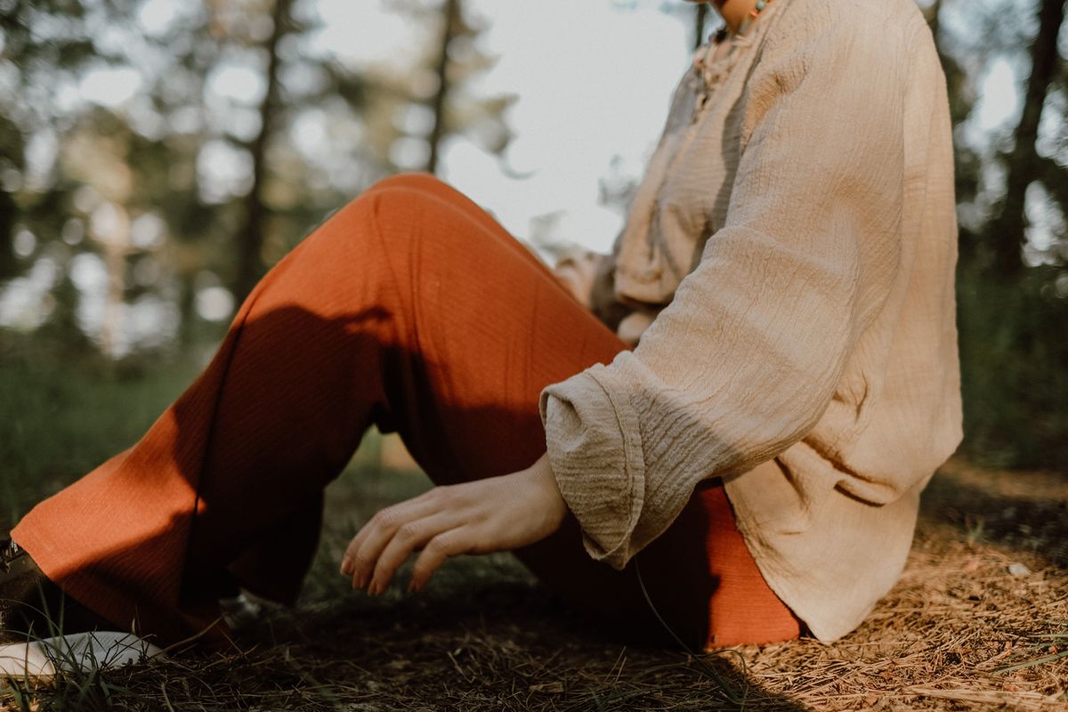 A woman sitting outdoors wearing red pants and cream shirt, enjoying nature.