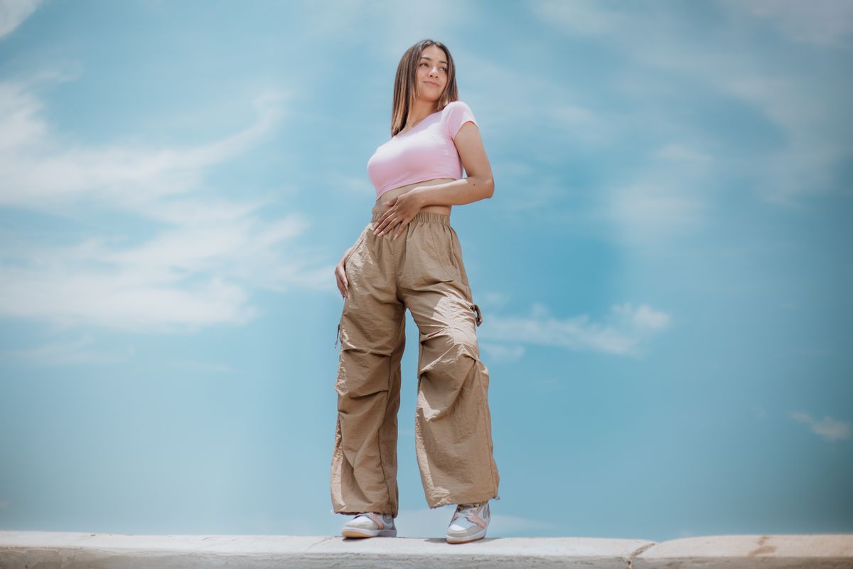 Woman posing outdoors in casual clothing against a bright sky, showcasing modern fashion trends.