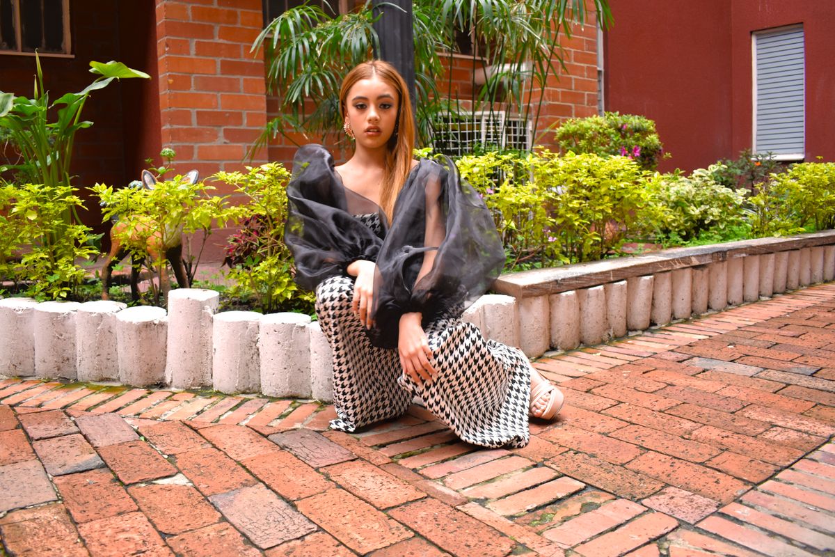 Stylish woman in bold outfit poses in vibrant garden area, showcasing modern fashion.