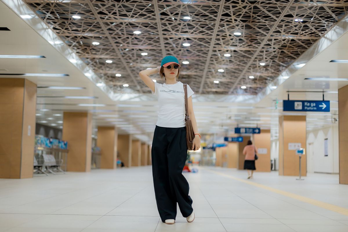 Woman wearing stylish outfit and sunglasses walking in a bright modern station.