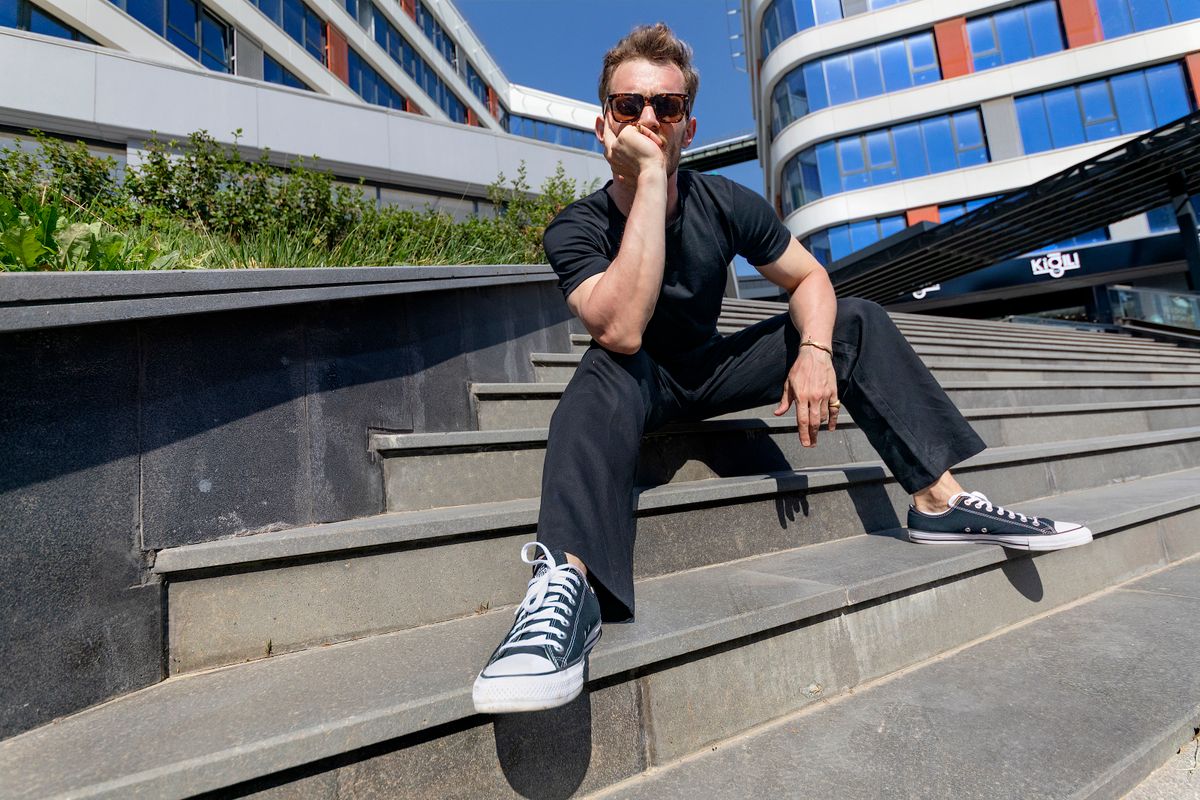 Casual portrait of a man sitting on steps in an urban setting, wearing sunglasses and casual attire.