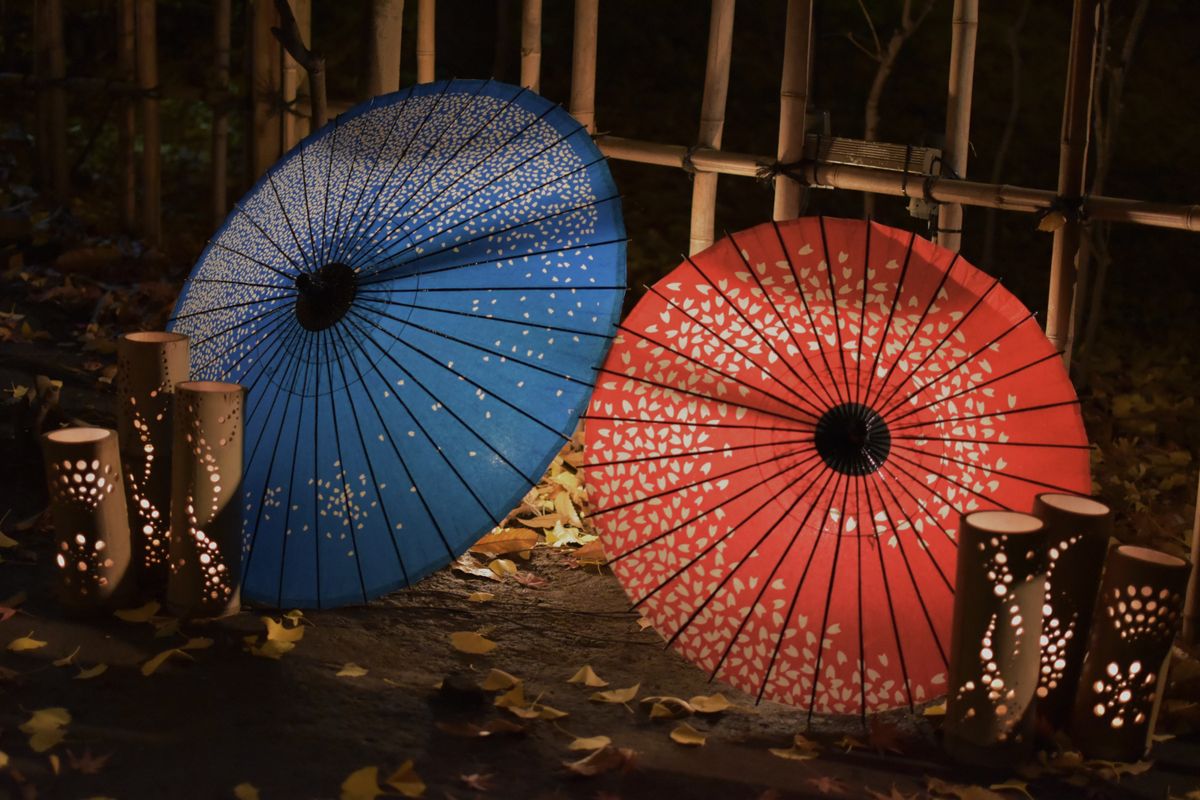Decorative blue and red Japanese umbrellas with illuminated bamboo lanterns at night.