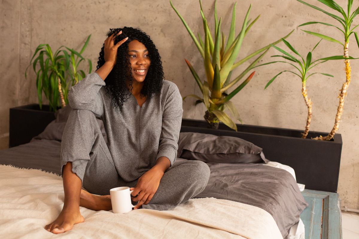 Relaxed woman with curly hair enjoying coffee indoors, wearing cozy gray pajamas.