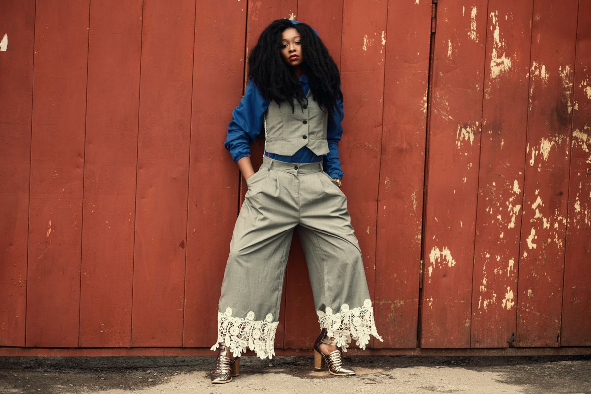 Stylish woman posing in a chic outfit against a rustic red wall in an urban setting.