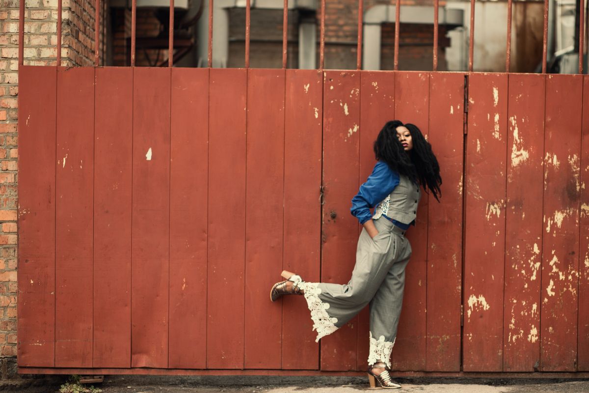 Fashionable woman posing against a vibrant red gate in an urban setting, showcasing modern style.