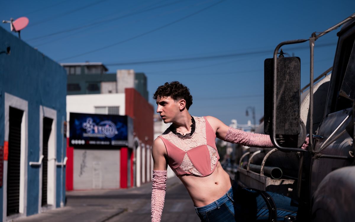 A young man wearing trendy fashion poses confidently near an industrial vehicle on a city street.