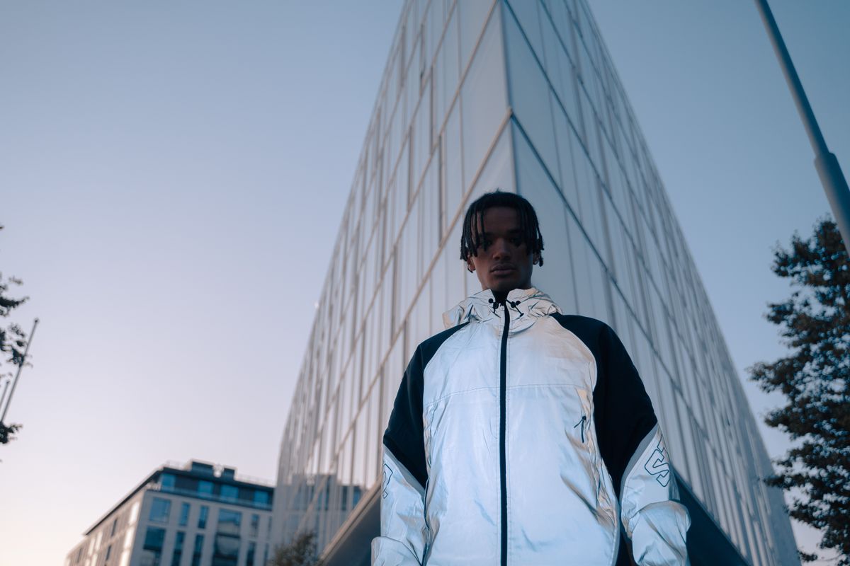 Stylish urban portrait of a man in a reflective jacket against a modern building backdrop.
