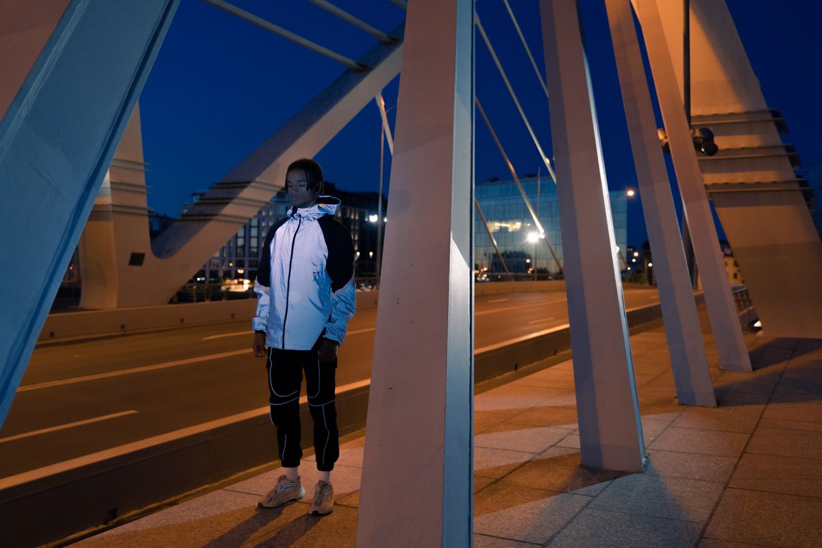 A man in a reflective jacket standing on a modern bridge during twilight, showcasing urban architecture.