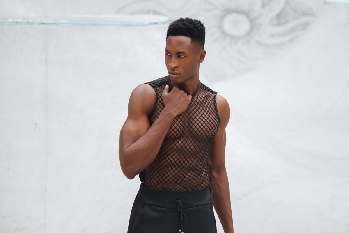 Portrait of a stylish man in a mesh top posing outdoors, showcasing modern fashion and attitude.
